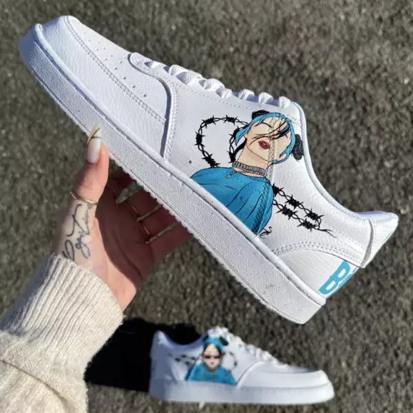 Nike custom Billie Eilish bleue avec portraits peints à la main, barbelés noirs autour des swoosh et inscriptions "Billie" et "Eilish" à l’arrière. Modèle visible : Nike Court Vision Low.