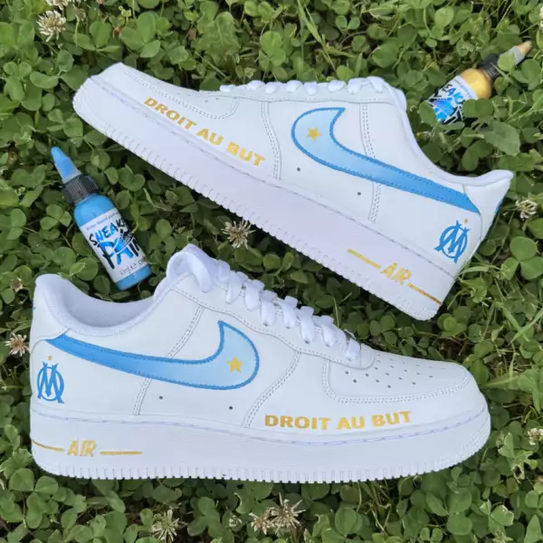 Nike Air Force 1 custom OM avec swoosh dégradé bleu et blanc, étoile dorée, logo de l’Olympique de Marseille à l’arrière, et inscription “DROIT AU BUT” en doré à l’avant.